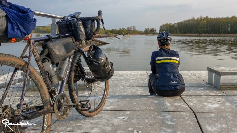 Radelmaedchen sitzt am Wasser mit Fahrrad im Vordergrund