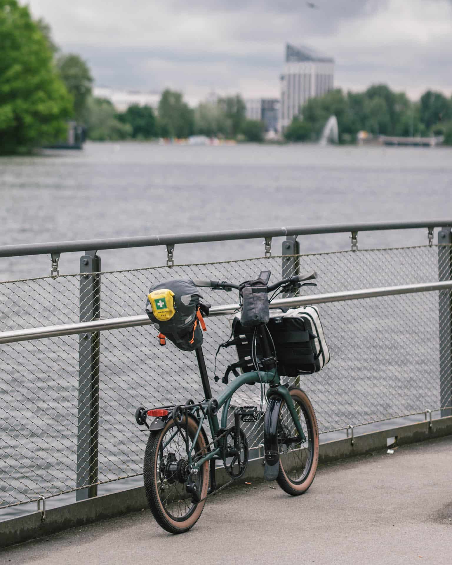 Brompton am See an Geländer gelehnt mit Gepäck am Rad
